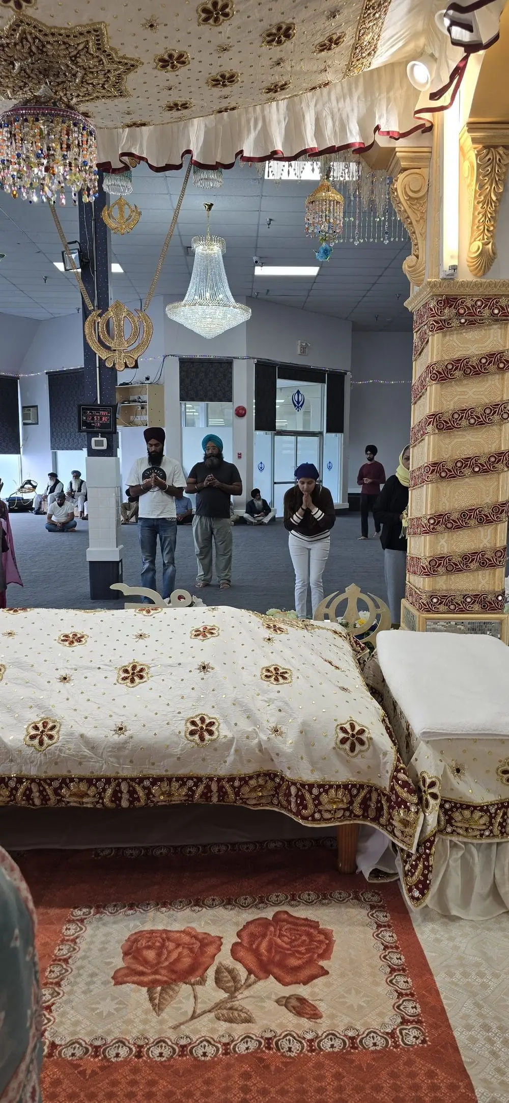 Interior view of the Darbar Sahib with decorated palki, chandeliers, and worshippers praying.