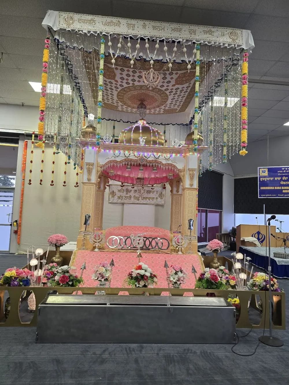 Central decorated palki structure under hanging ornaments in the prayer hall.