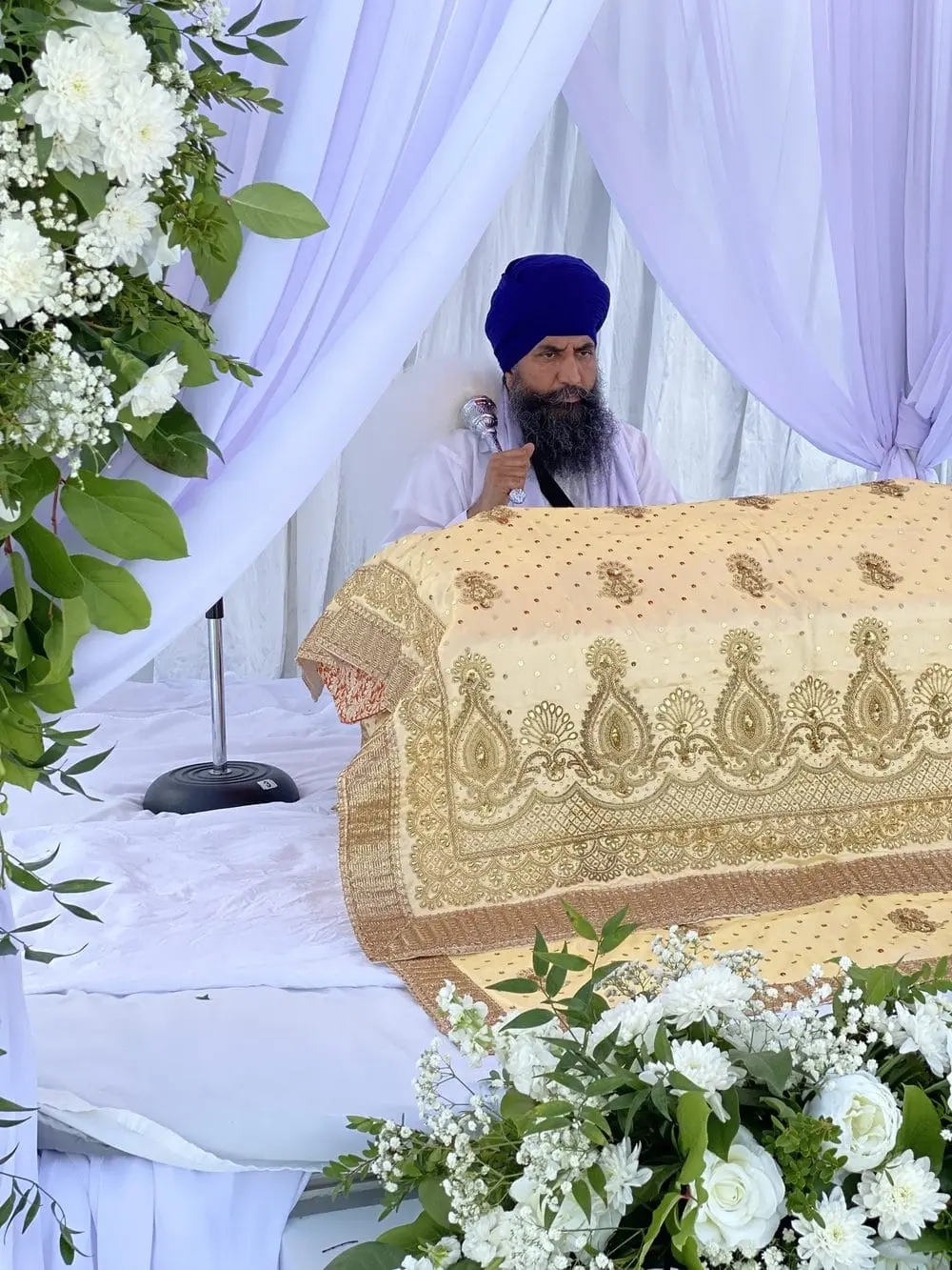 Close-up of embroidered rumala cloth with a granthi in the background.