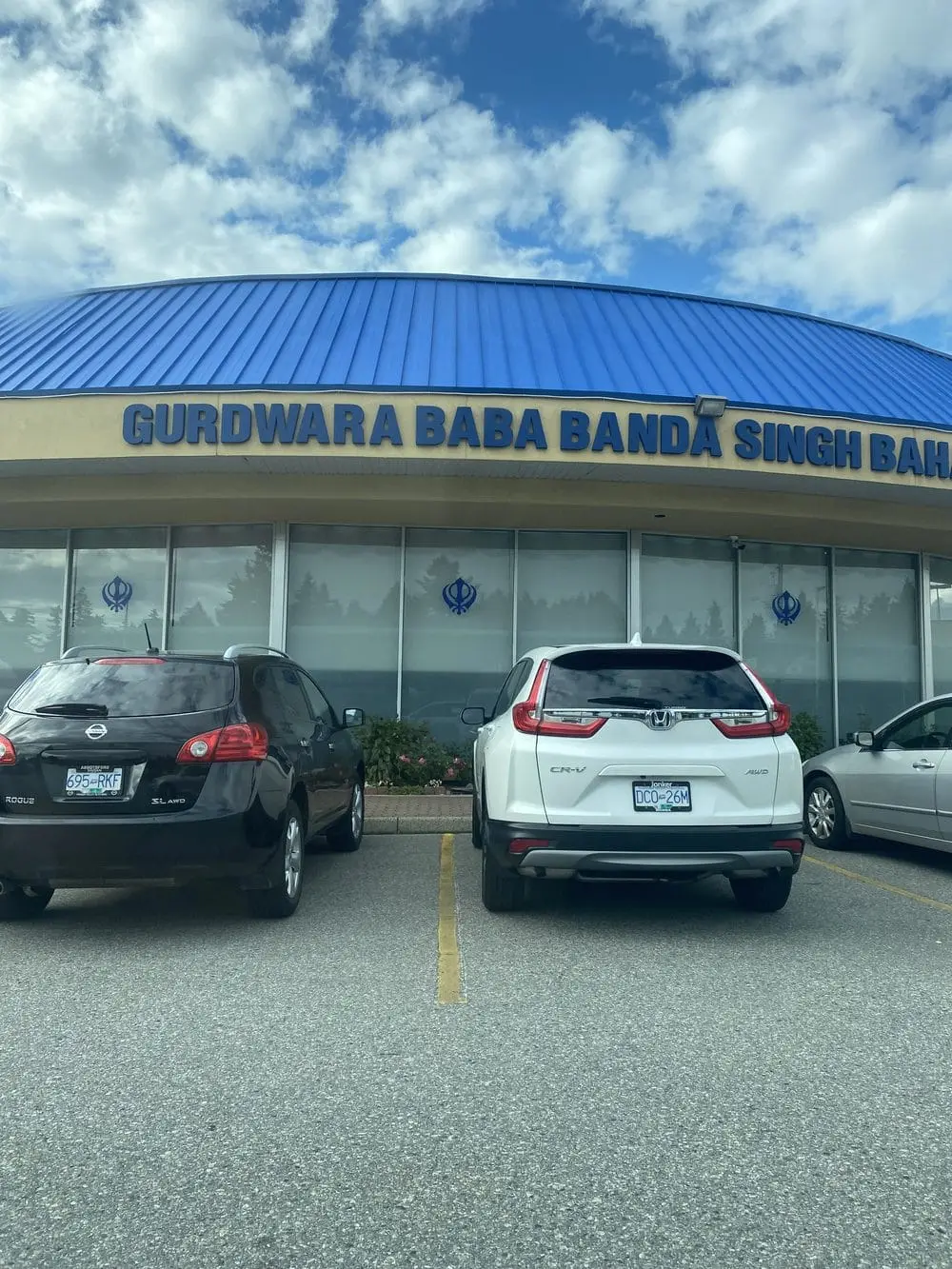 Front exterior signage of the Gurdwara building with parked vehicles.