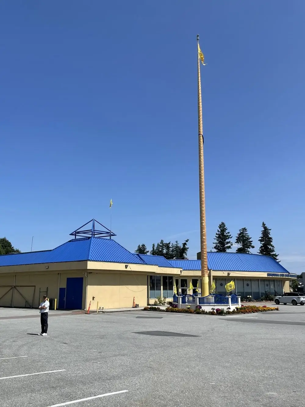 Wide exterior of the blue-roof Gurdwara building and Nishan Sahib pole.