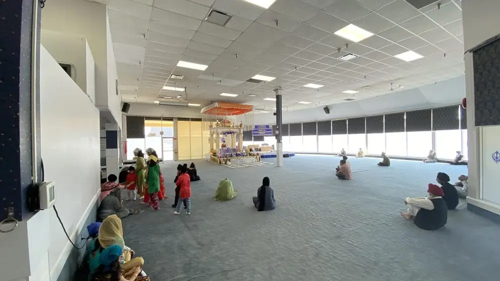 Wide prayer hall with children and worshippers seated along the sides.